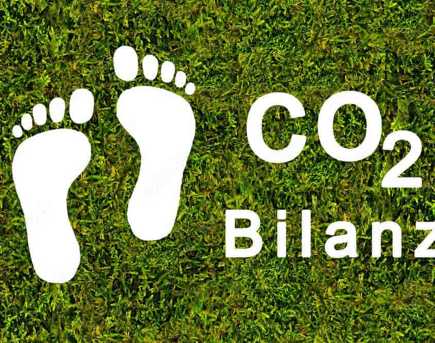 Grüner Rasen mit weißen Abdrucken von einem Paar Füße und der Schrift CO2 Bilanz