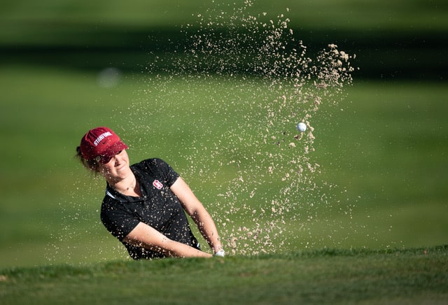 Foto der College-Golferin Rebecca Becht im Bunker. Der Sand spritzt heraus.