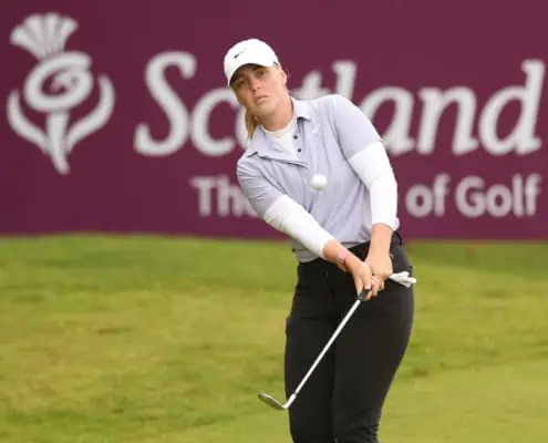 Bild auf eine Spielerin beim Chip vor einem Plakat von Scotland Golf