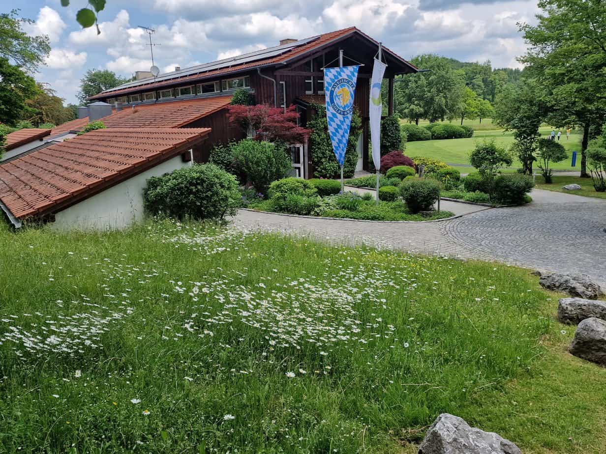 Blick auf eine bunte Blumenwiese vor einem Clubhaus mit einer Bayern-Fahne