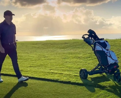 Golfer geht hinter einem Trolley mit Golfbag