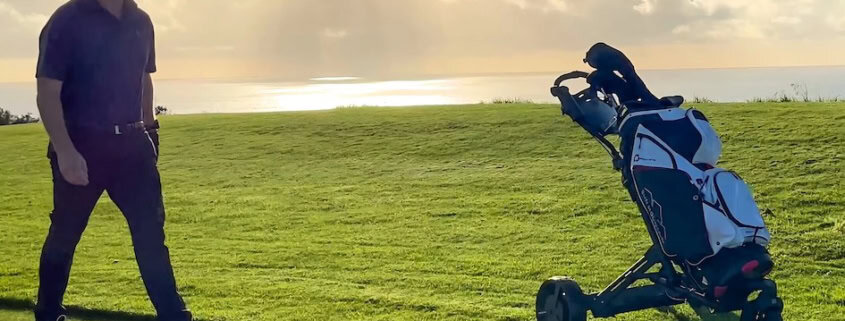 Golfer geht hinter einem Trolley mit Golfbag