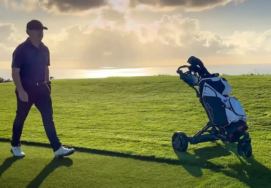 Golfer geht hinter einem Trolley mit Golfbag